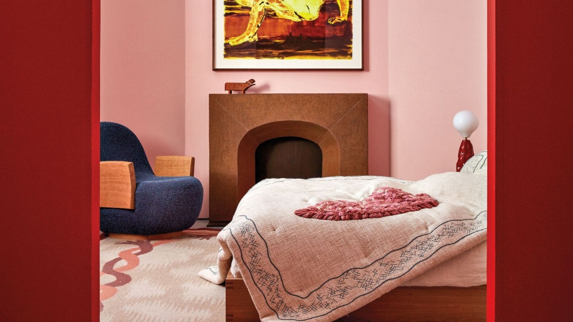 Bedroom with pink walls, modern art, cozy armchair, textured bedspread, and minimalist decor.