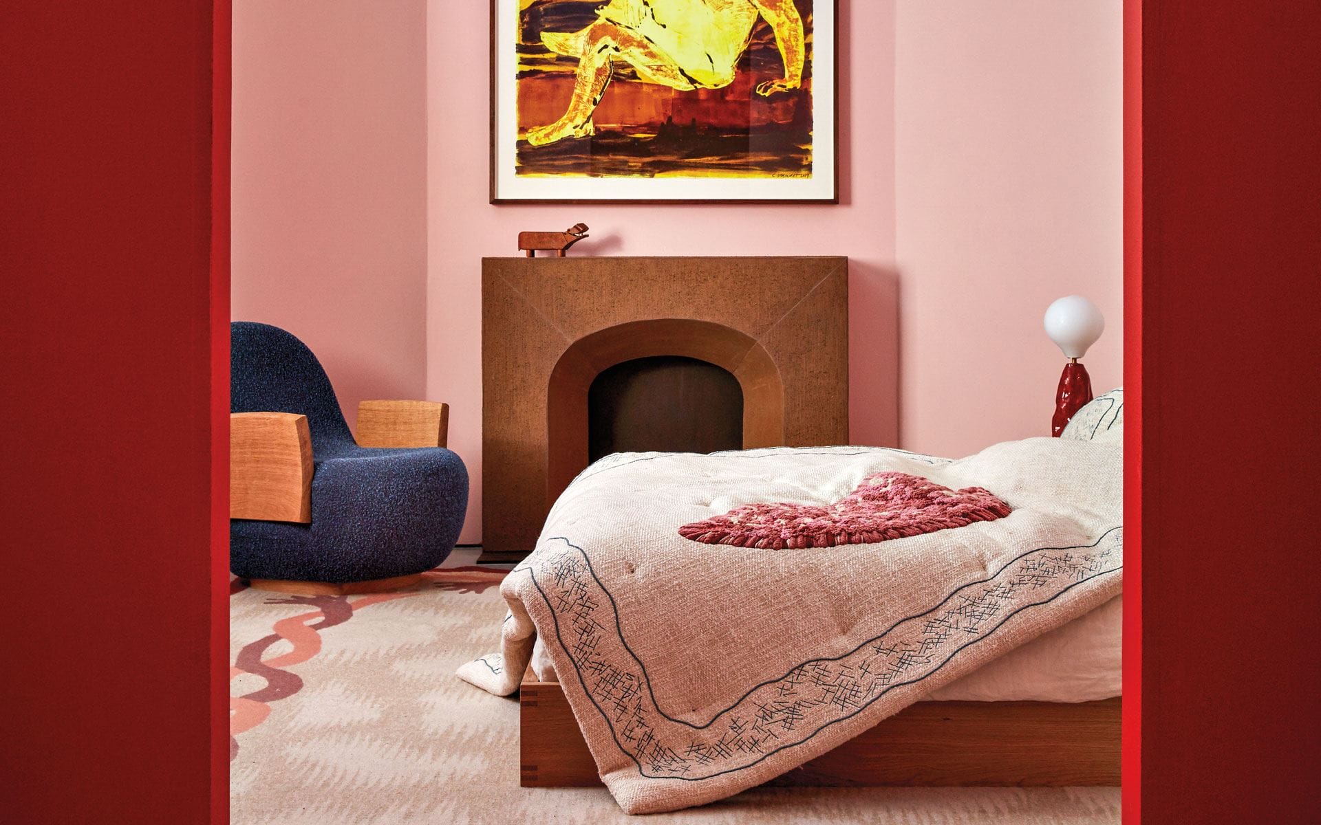 Bedroom with pink walls, modern art, cozy armchair, textured bedspread, and minimalist decor.