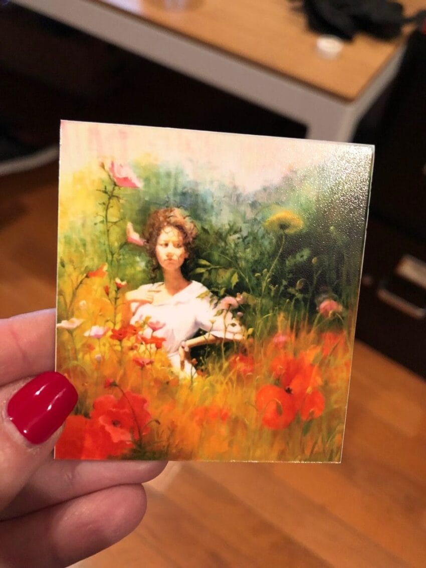 Painting of a woman with curly hair surrounded by colorful flowers held by a person with red nail polish.
