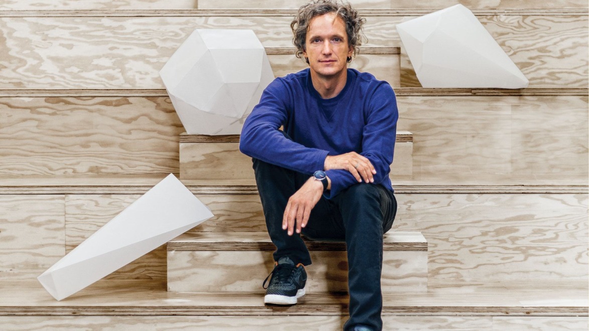 Man sitting on wooden steps surrounded by abstract white geometric sculptures.