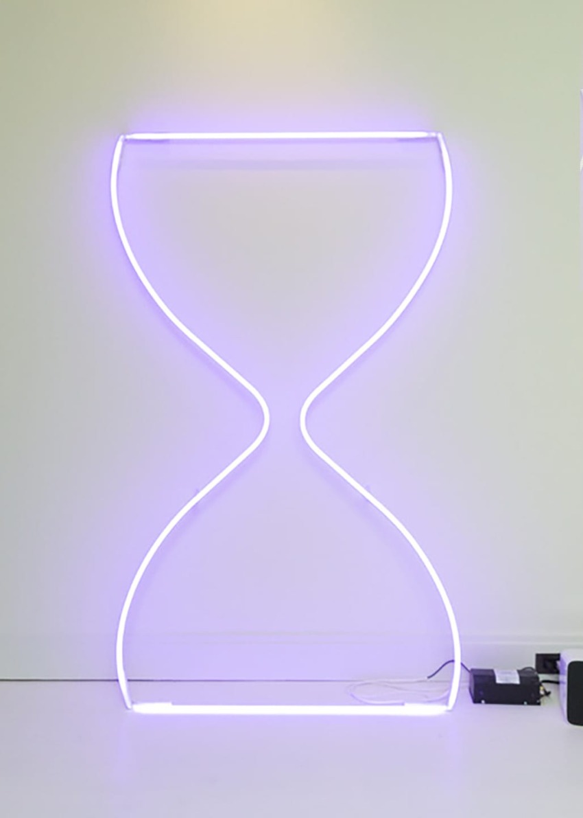 Purple neon hourglass-shaped light installation against a white wall.