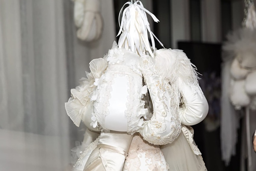 Person wearing elaborate, artistic white costume with feathers and lace, displaying unique fashion design.