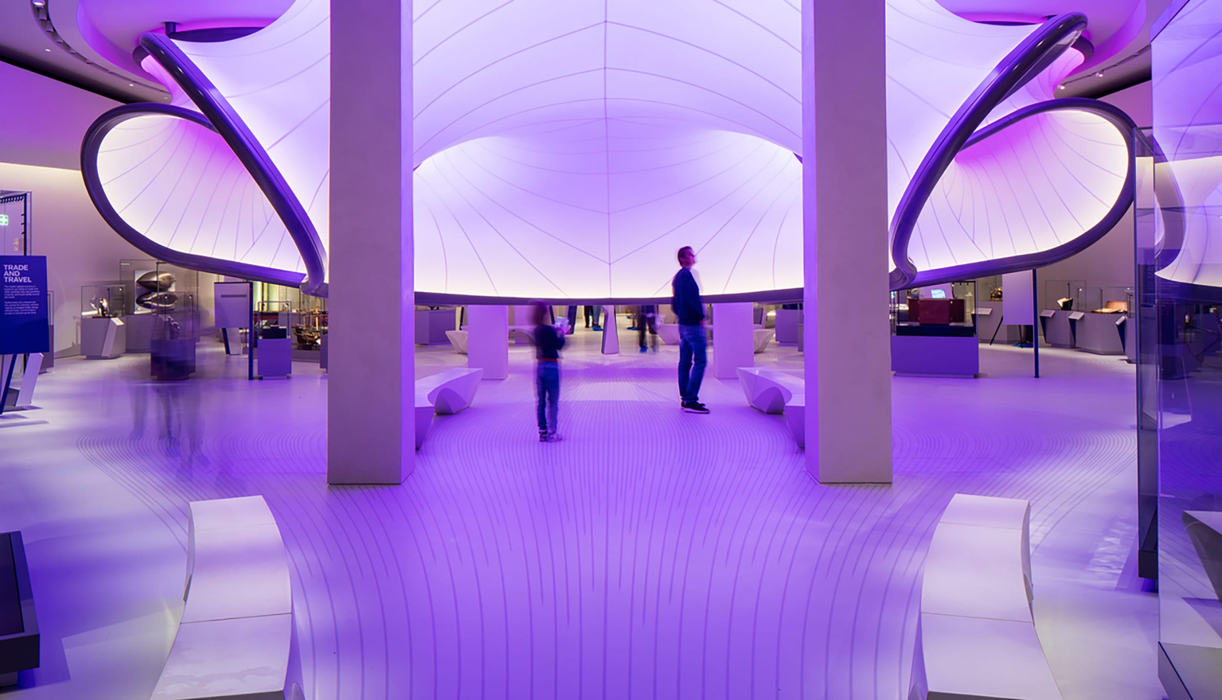 People in a futuristic exhibition space with purple lighting and curved architectural design.