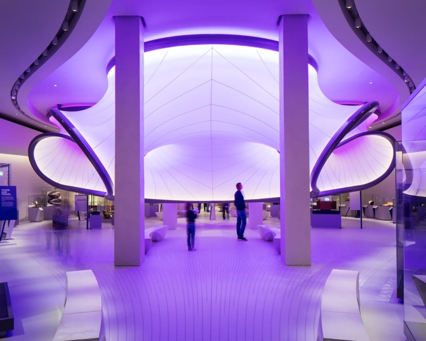 Futuristic, purple-lit exhibition space with sleek design, curved architecture, and people walking around.