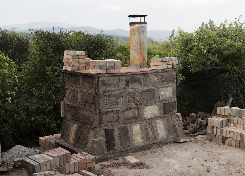 Rustic brick barbecue smoker under construction in an outdoor setting with trees and mountains in the background.