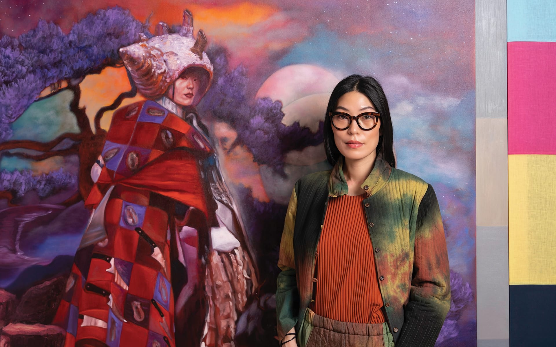 Person standing in front of a colorful painting featuring a surreal figure, wearing glasses and a vibrant outfit.