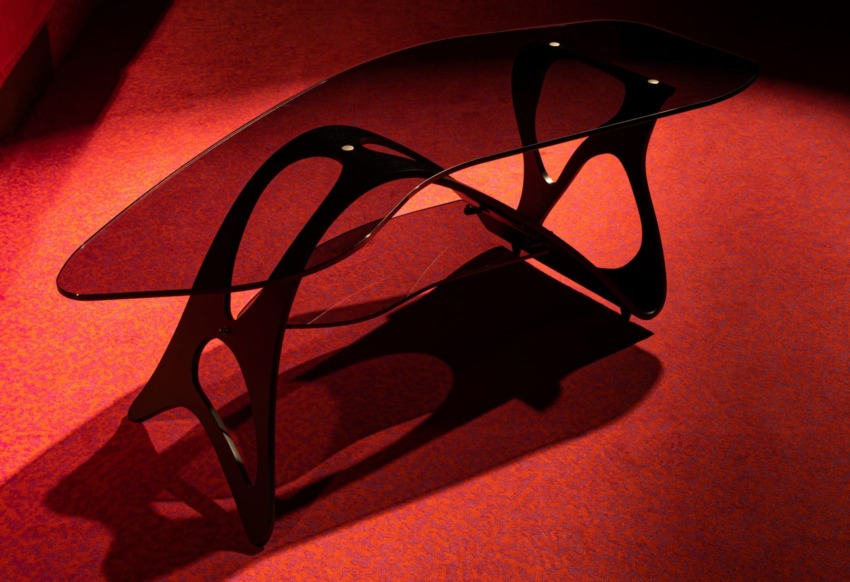 Modern glass coffee table with a sleek black frame on a red carpeted floor.