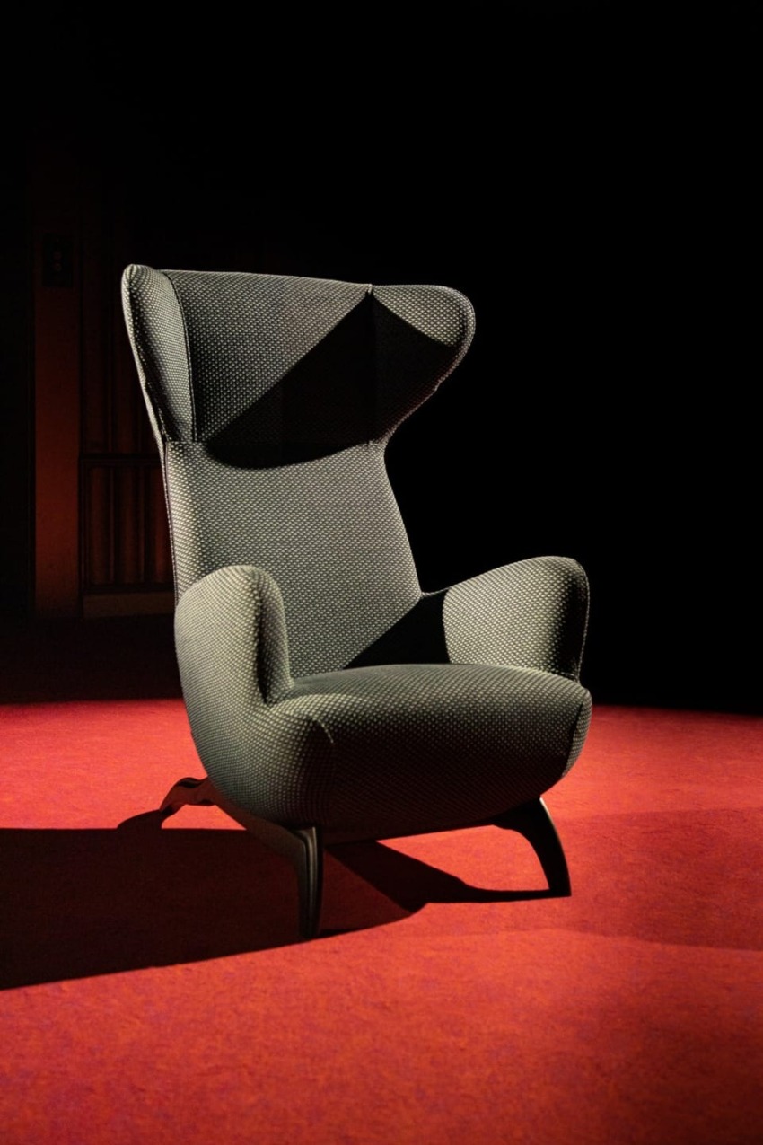 Modern high-back chair with textured fabric upholstery on a red carpeted floor with a dark background.