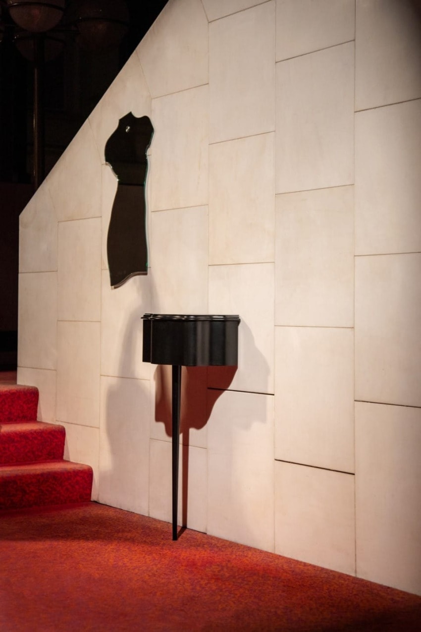 Stylish wall-mounted black dress silhouette art above a small black console table on a red carpeted staircase landing.