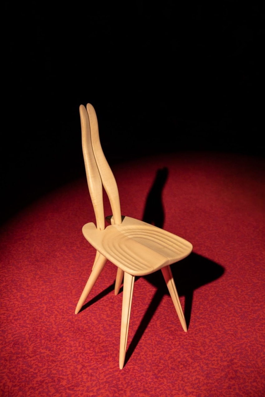 Wooden designer chair with elongated backrest on a red carpet.