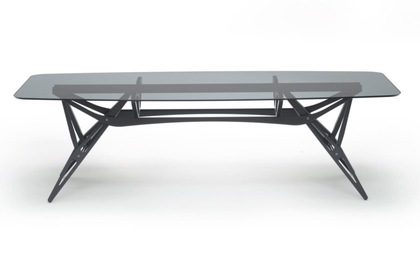 Modern glass-top table with sleek black metal frame and geometric legs, viewed from an angle.