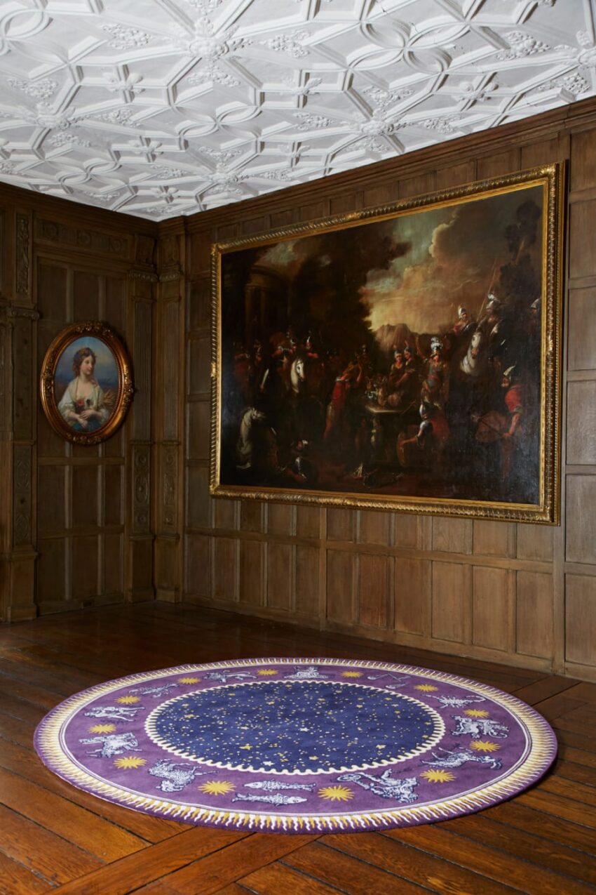 A room with wood paneling, two framed paintings on the walls, and a circular purple rug on the wooden floor.
