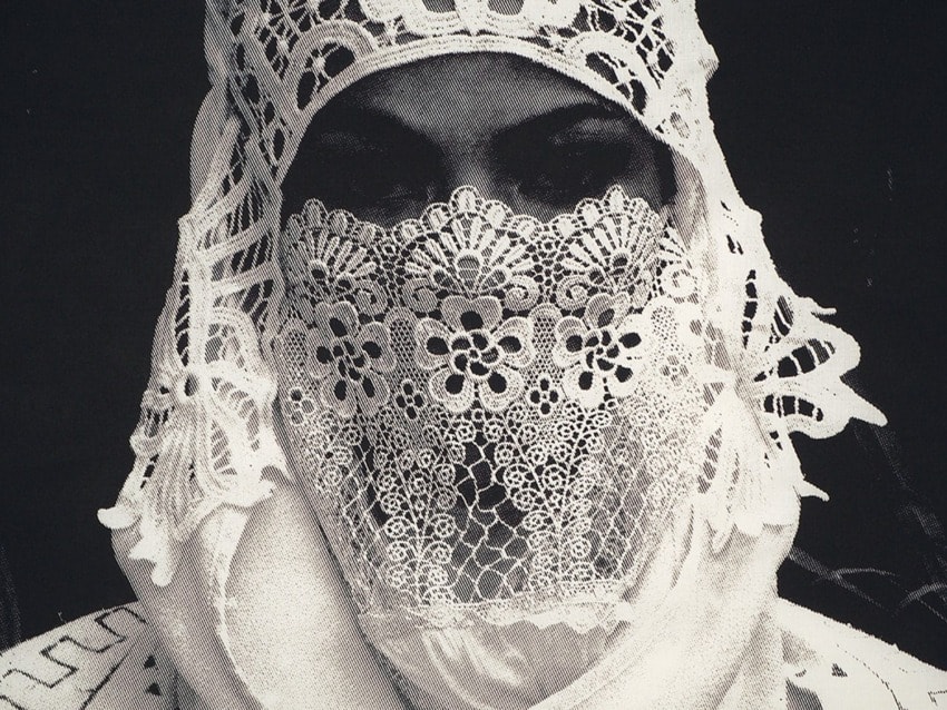 Person wearing intricate white lace head covering and veil in a black and white image.