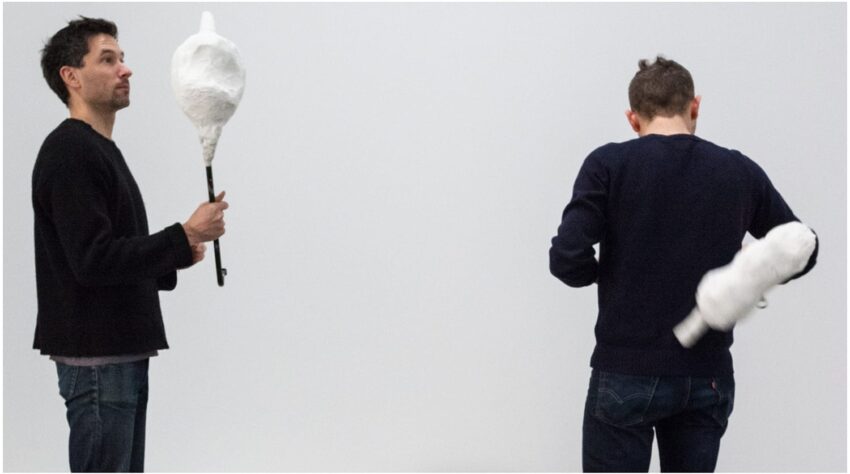 Two people holding and interacting with abstract white sculptures against a plain background.