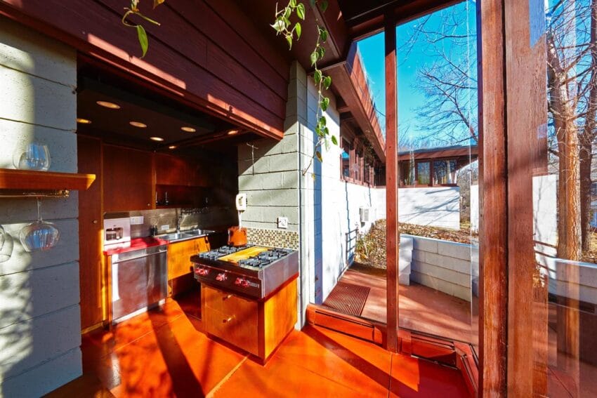 Bright kitchen with wooden cabinets, large windows, and view of an outdoor area on a sunny day.