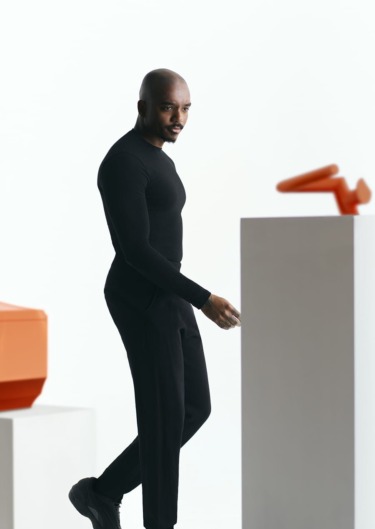 Person in black outfit standing beside modern art sculptures in a minimalistic gallery space.
