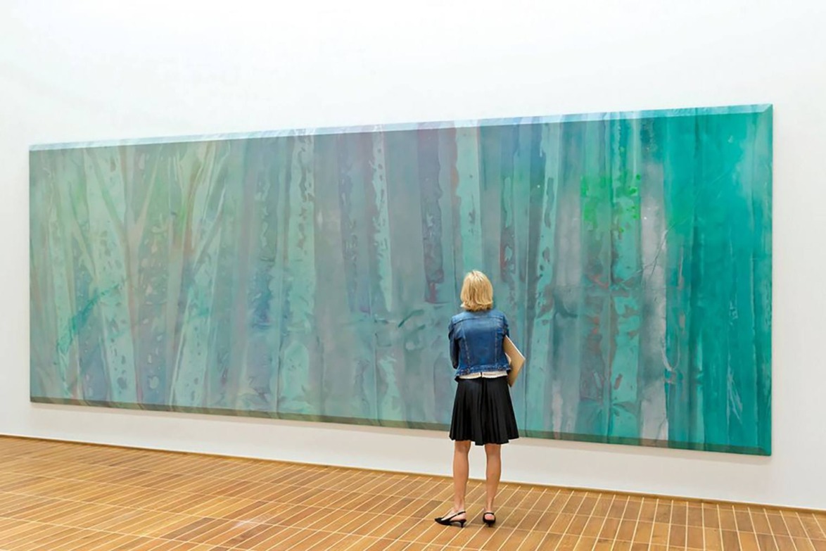 Person standing in front of a large abstract painting with green and blue tones in a gallery setting.