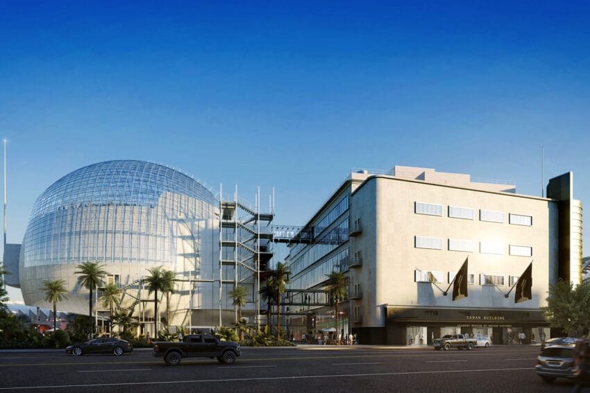 Modern building with a glass dome and palm trees, cars on the street, clear blue sky background.