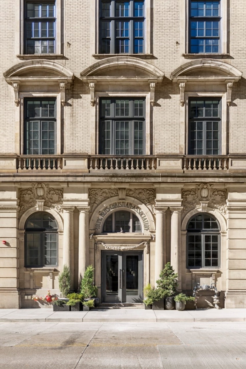 Historic building facade with ornate architecture, large windows, and decorative entrance surrounded by potted plants.