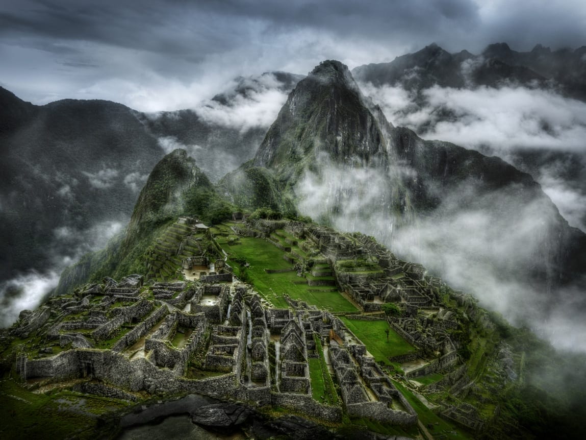 Aerial view of Machu Picchu ruins surrounded by misty mountains and clouds.