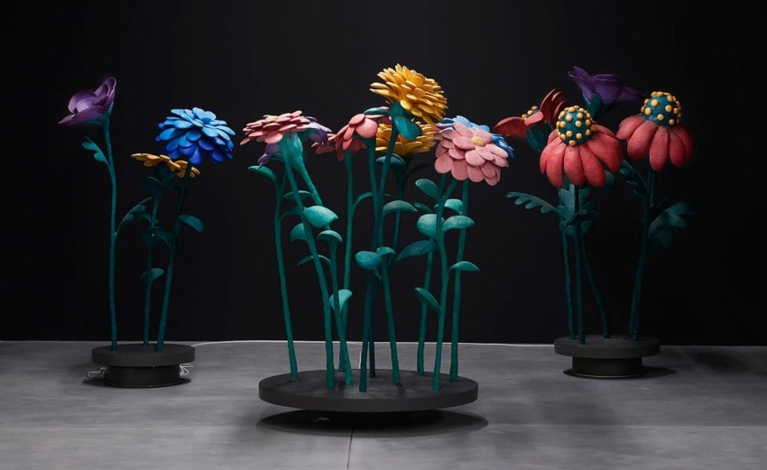 Colorful large flowers on rotating platforms in a dark room, creating an artistic and whimsical display.