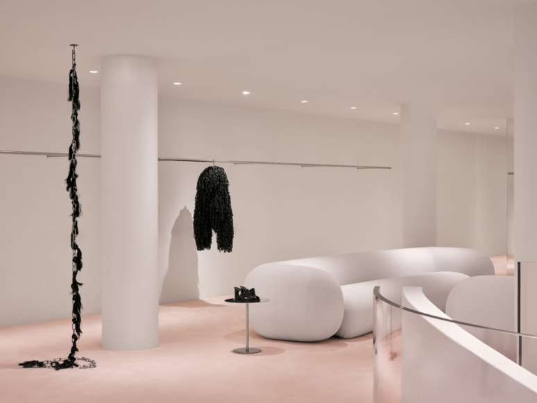 Modern minimalist room with white couch, black sculpture, hanging art, and a small table on a pink floor.
