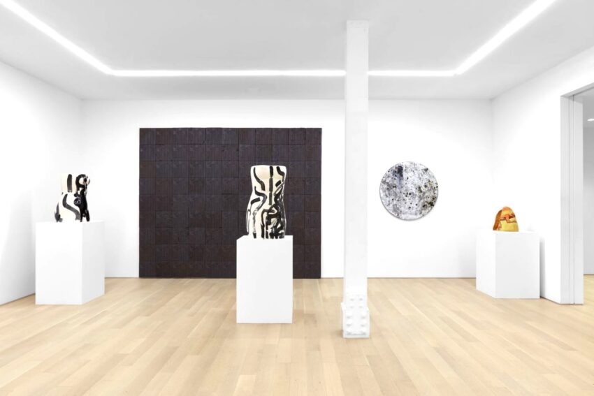 Modern art gallery interior with sculptures on pedestals and abstract wall art, featuring minimalistic white walls and wood flooring.