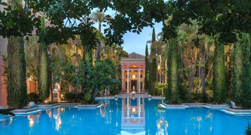 Luxurious outdoor pool surrounded by lush greenery and tall columns at a grand resort with a serene ambiance.