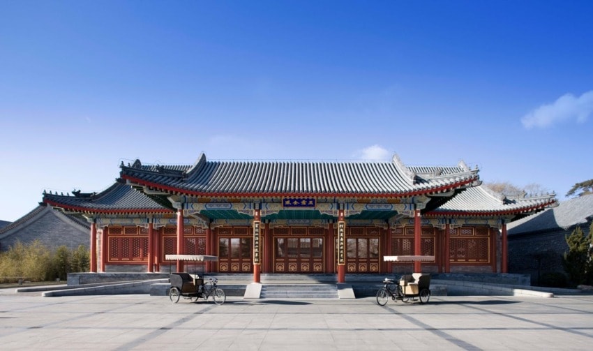 Traditional Chinese building with ornate details and a clear blue sky, featuring two rickshaws in front.