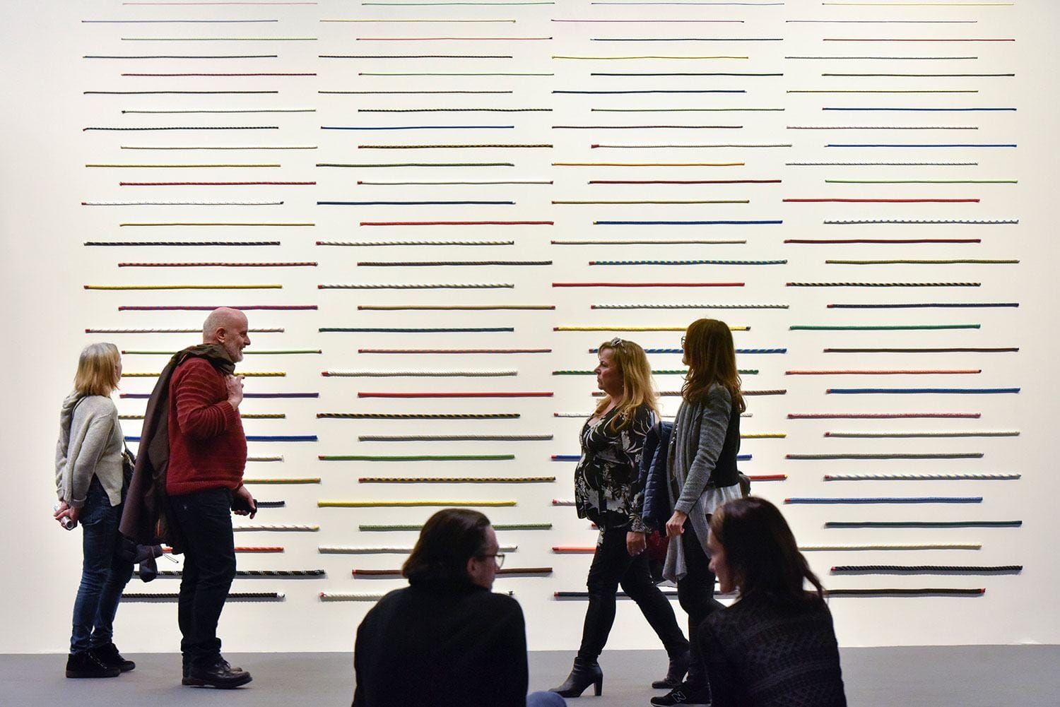People viewing a colorful modern art installation with horizontal lines in a gallery setting.