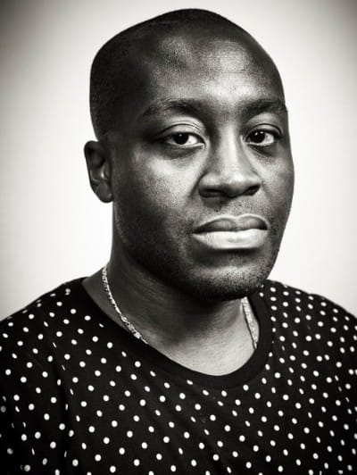 Man wearing a polka-dot shirt, looking directly at the camera with a neutral expression, black and white portrait.