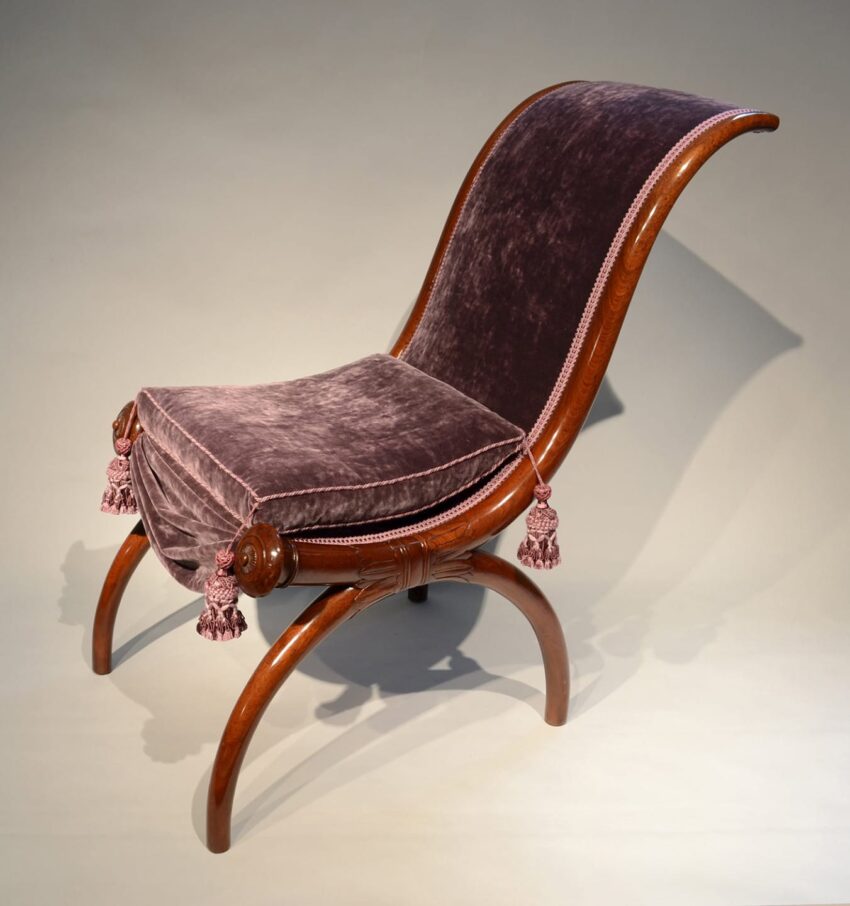 Antique wooden reclining chair with velvet upholstery and decorative tassels on a curved leg design.