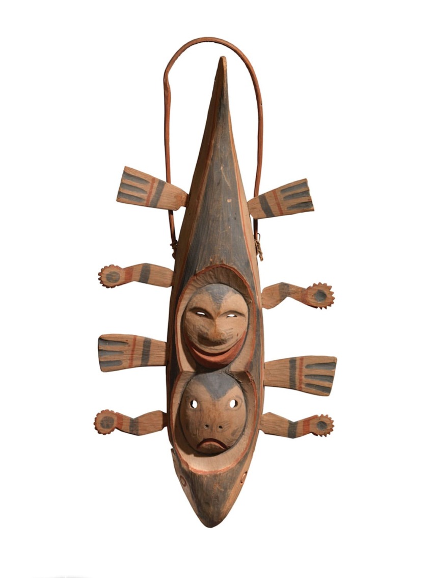 Traditional carved wooden sculpture with human faces and intricate details, featuring a canoe-like shape and six paddle-like limbs.