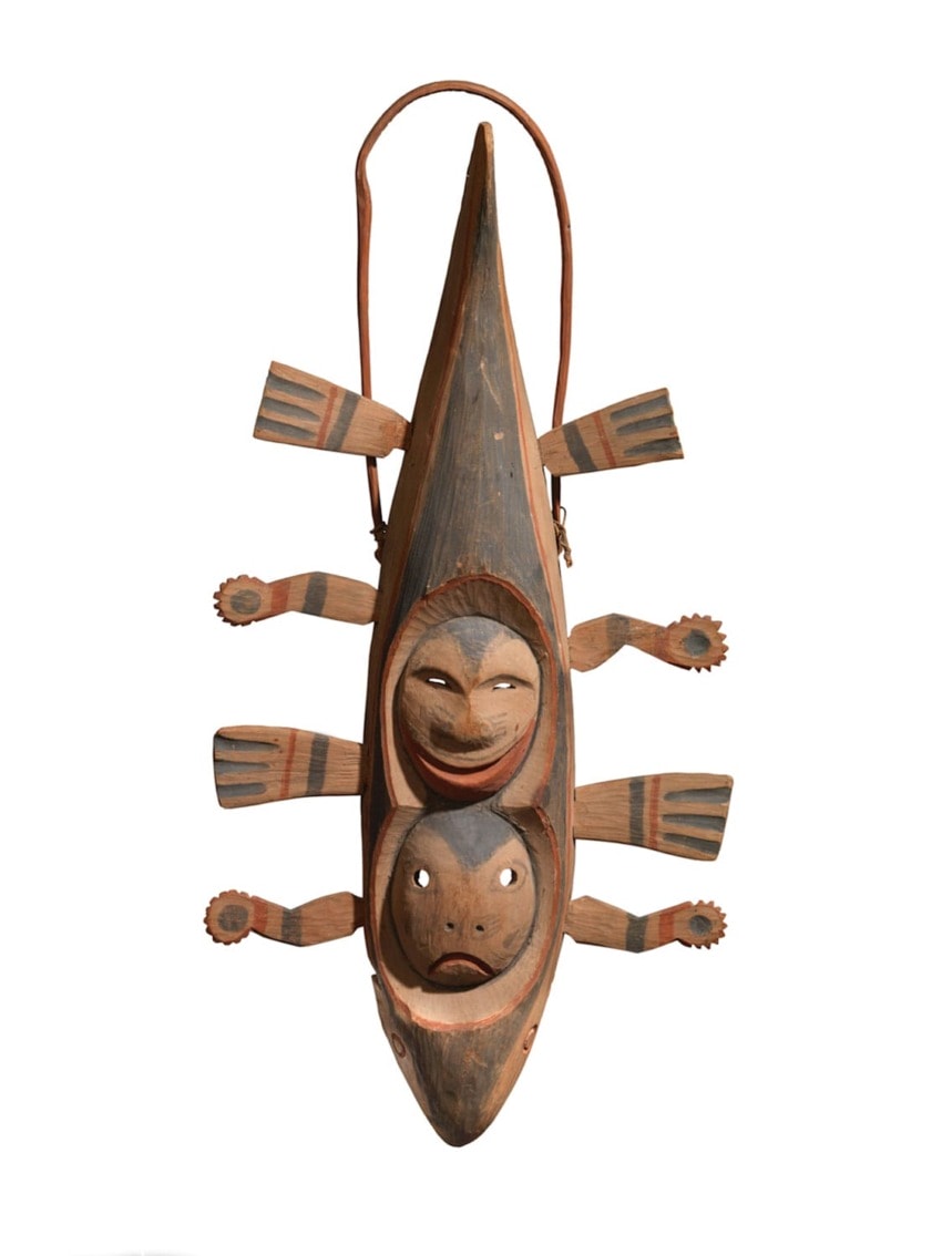 Traditional carved wooden sculpture with human faces and intricate details, featuring a canoe-like shape and six paddle-like limbs.