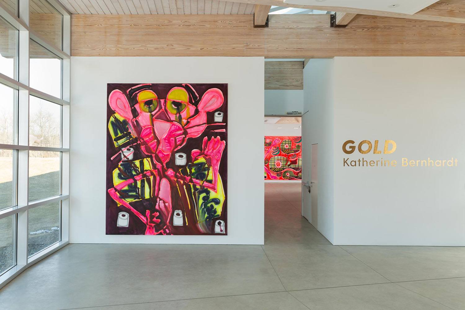 Colorful abstract painting in modern gallery with "GOLD Katherine Bernhardt" displayed on adjacent wall.