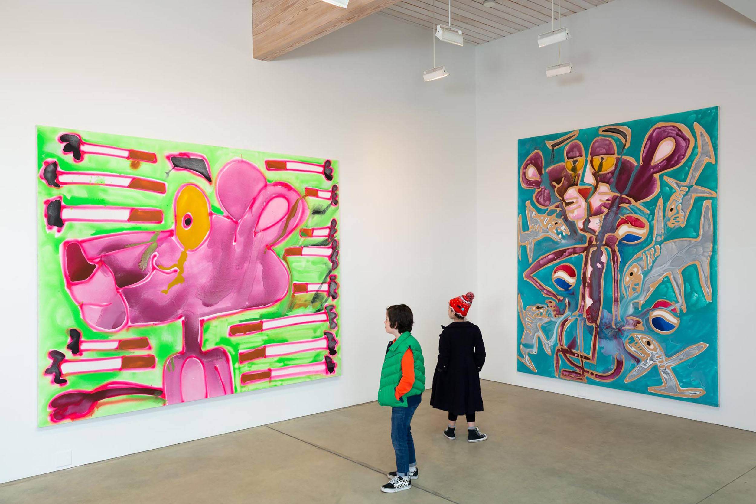 Two people viewing colorful abstract art paintings in a modern gallery with high ceilings and minimalist design.