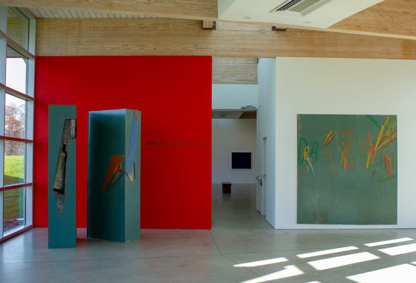 Modern art gallery interior with colorful abstract paintings and sculptures on display against red and white walls.
