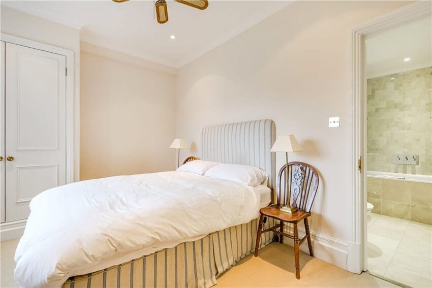 cozy bedroom with white bedding, wooden chairs, soft lighting, and an open door leading to a tiled bathroom