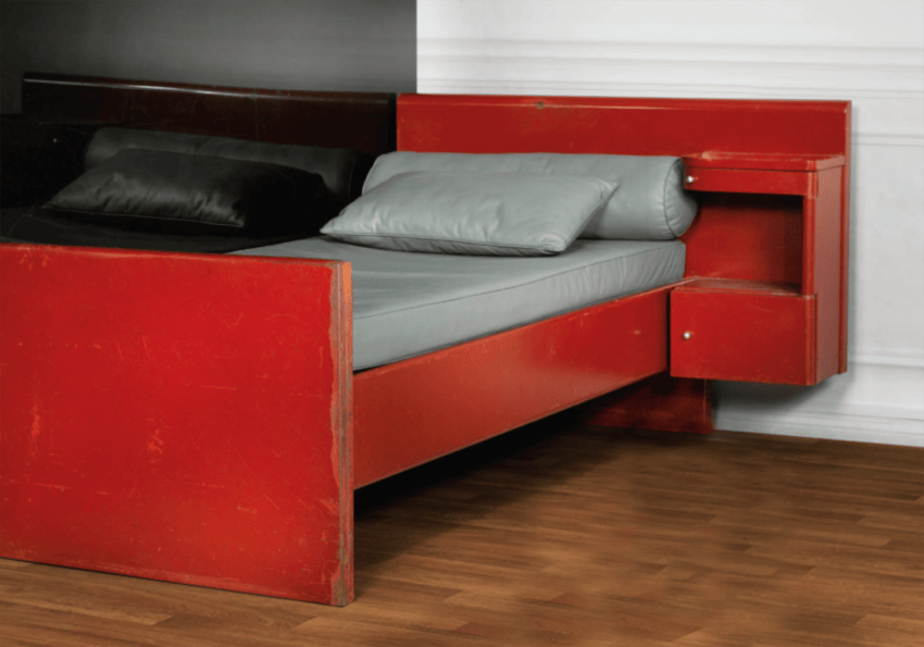 Red vintage bed with built-in side drawers and a gray mattress, located on a hardwood floor.