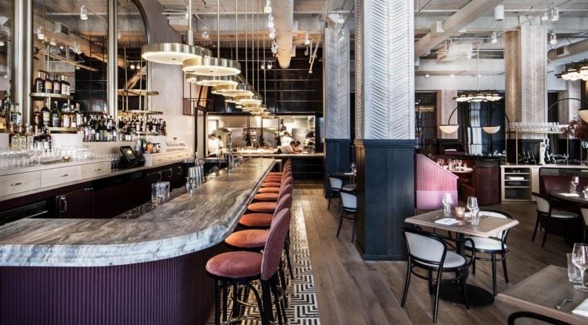 Contemporary restaurant interior with a marble bar, stylish seating, and an open kitchen in the background.