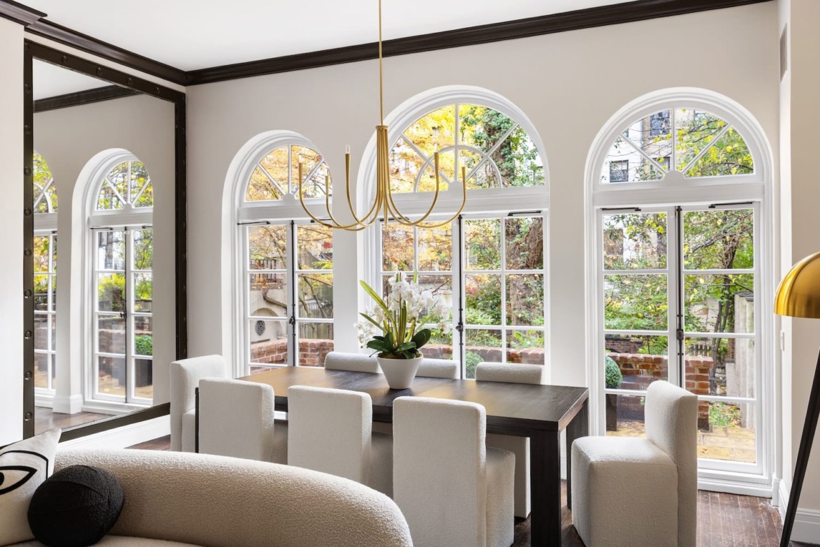 Elegant dining room with large arched windows, white chairs around a dark wooden table, and a modern chandelier.
