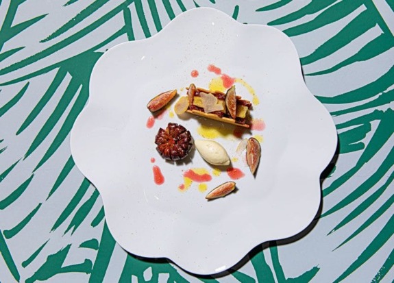 Gourmet dessert with mousse, pastry, and sauce on a decorative white plate with a green patterned background.