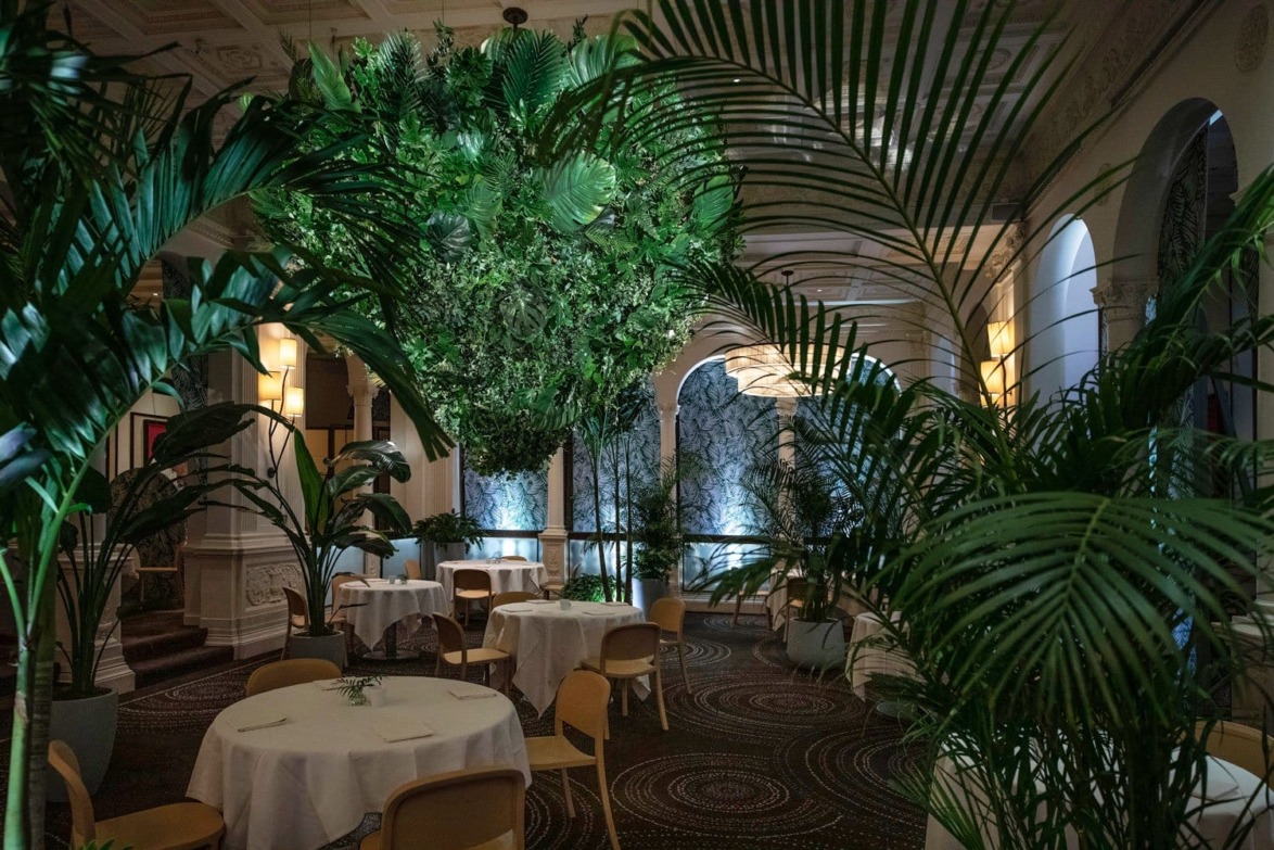 Elegant restaurant interior with lush greenery, round tables, and ambient lighting creating a serene dining atmosphere.