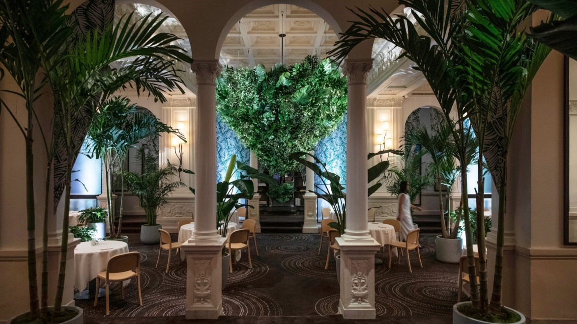 Luxurious dining area with elegant arches, lush greenery, and round tables set for guests in an ornate interior setting.