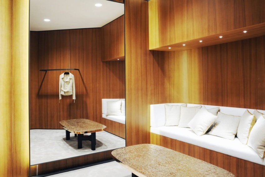 Modern dressing room with wooden walls, built-in bench, cushions, large mirror, and a hung white robe.
