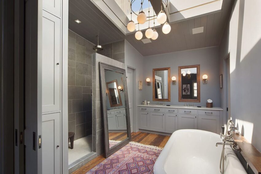 Modern bathroom with freestanding tub, large mirror, double sinks, and a walk-in shower, featuring overhead lighting.