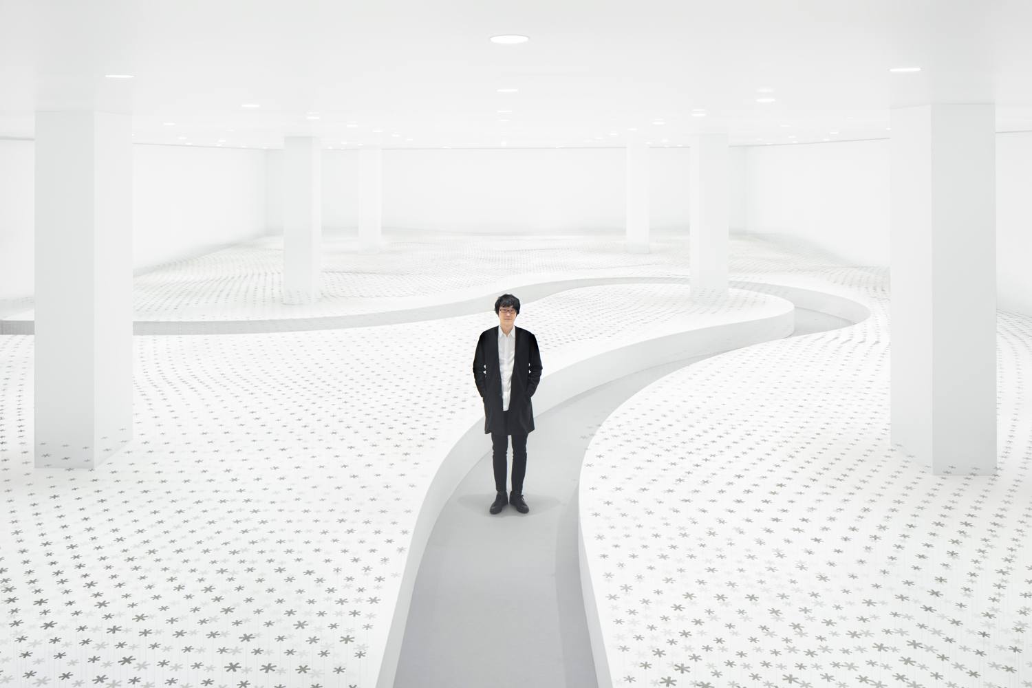 Person standing in a minimalist white room with winding path and patterned floor, surrounded by white walls and columns.