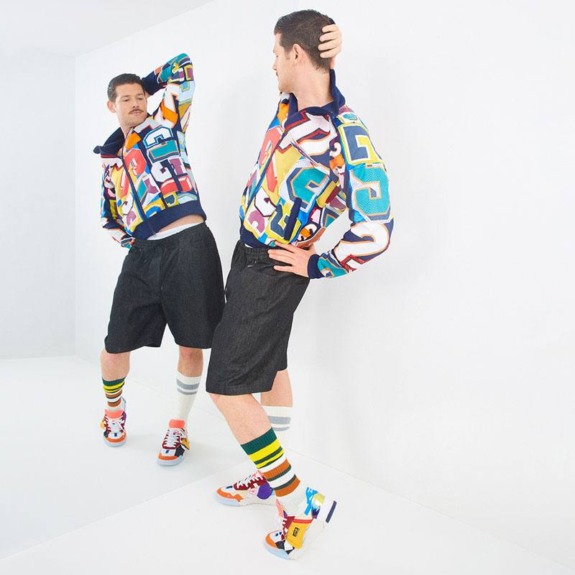 Two individuals in colorful geometric-pattern jackets and shorts, striking dynamic poses in a white space.