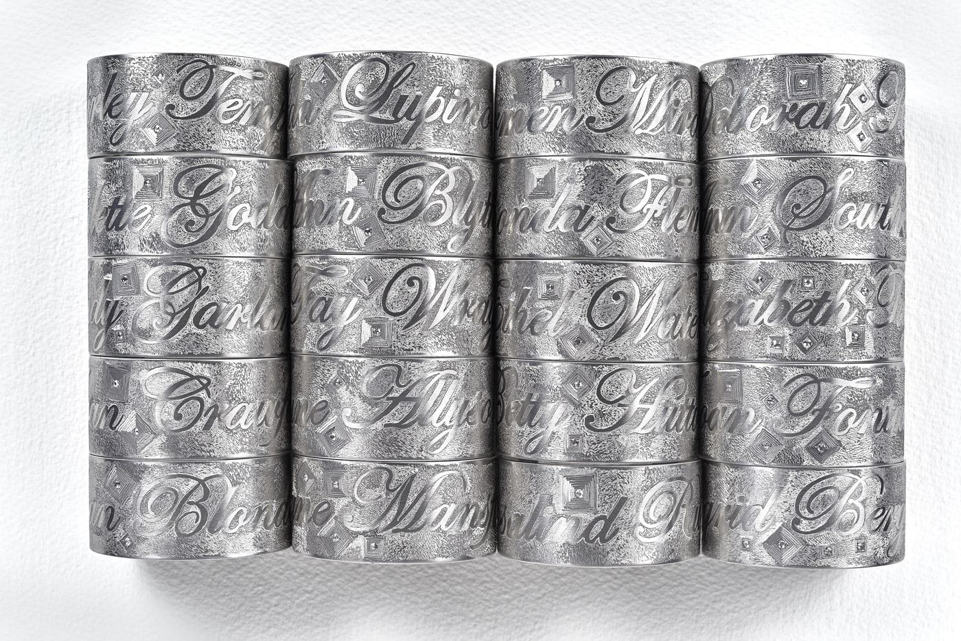Stack of intricately engraved silver rings on a white textured background arranged in a neat, orderly fashion.