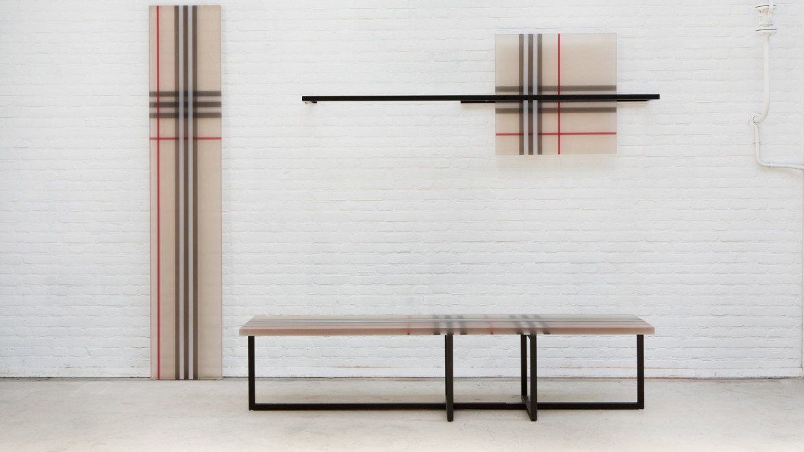 Contemporary art installation with linear patterns on panels and a bench against a white brick wall.